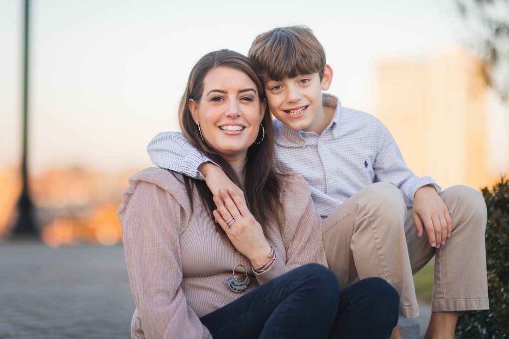 A woman and her son are sitting on the sidewalk in front of a building, enjoying a holiday together as a family.