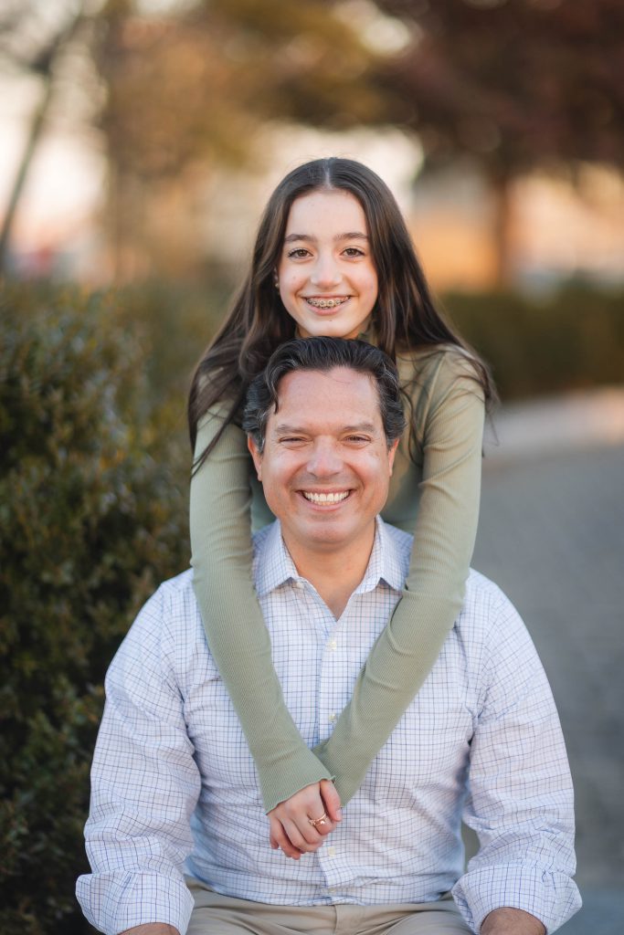 A man and his daughter are smiling while sitting on a bench at Federal Hill Park in Baltimore, creating beautiful portraits.