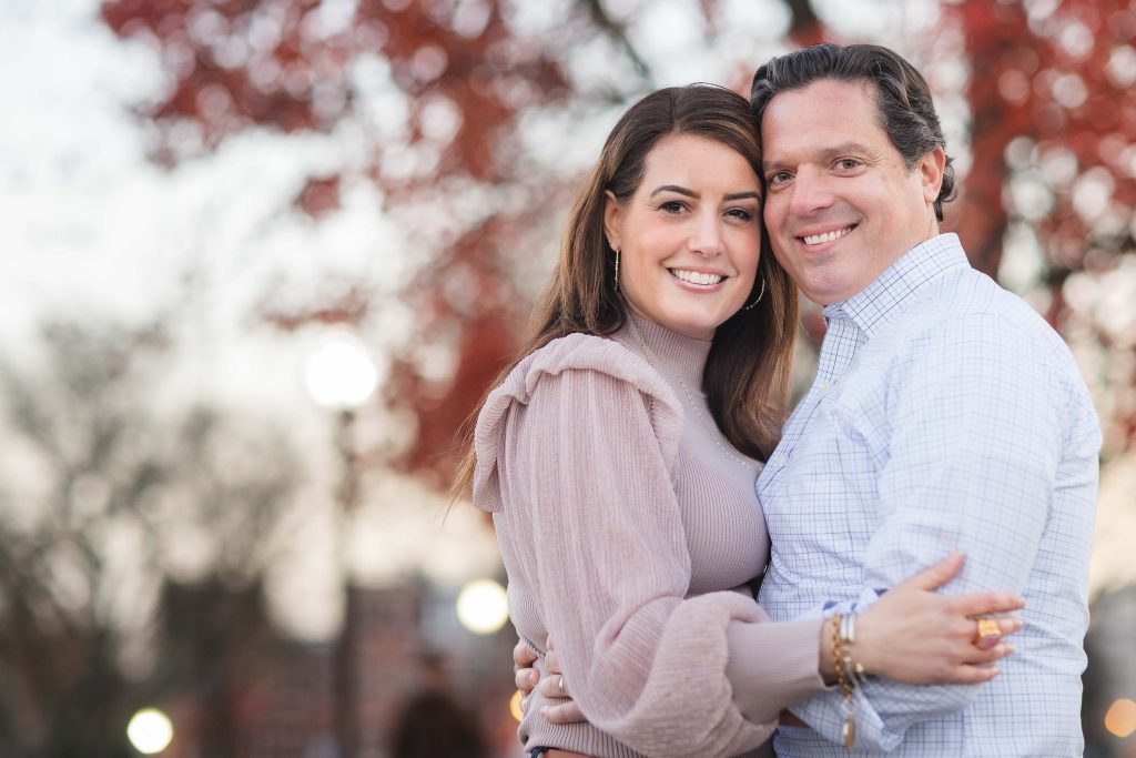 A couple embracing in front of a tree in a park during a holiday.