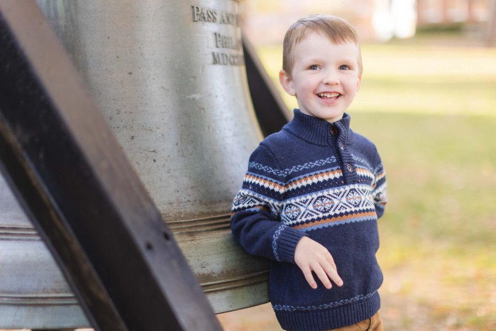 A young boy is leaning against a large bell in Downtown Annapolis.