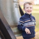 A young boy is leaning against a large bell in Downtown Annapolis.
