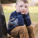 A young boy, sitting on a bench in downtown Annapolis, is captured in a portrait next to a bell.