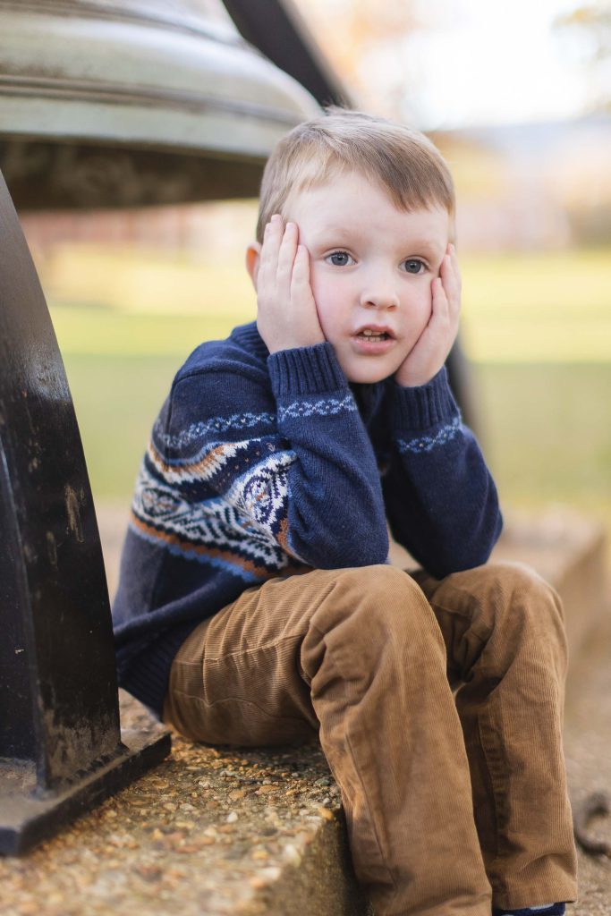 A young boy, sitting on a bench in downtown Annapolis, is captured in a portrait next to a bell.
