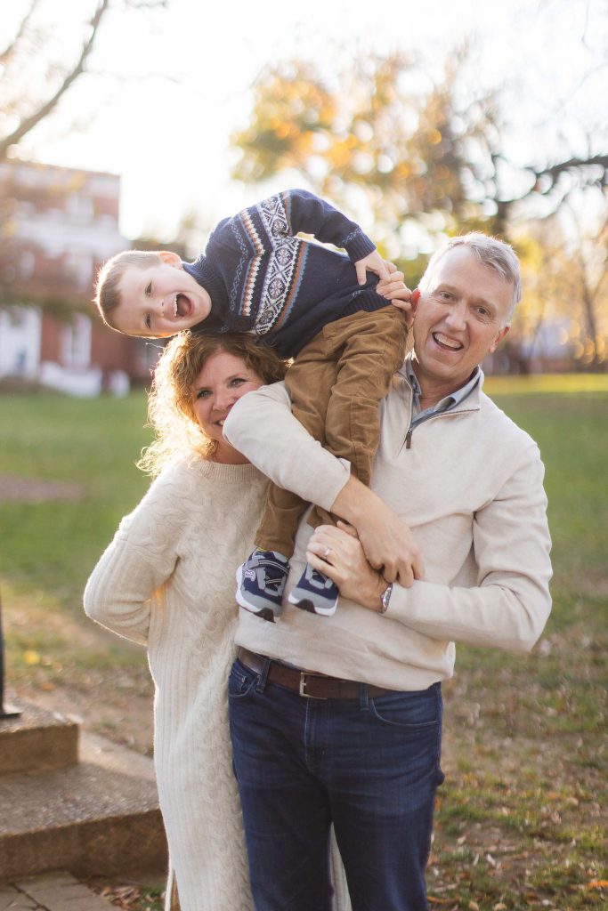A family is holding a young boy in their arms in a Downtown Annapolis park.
