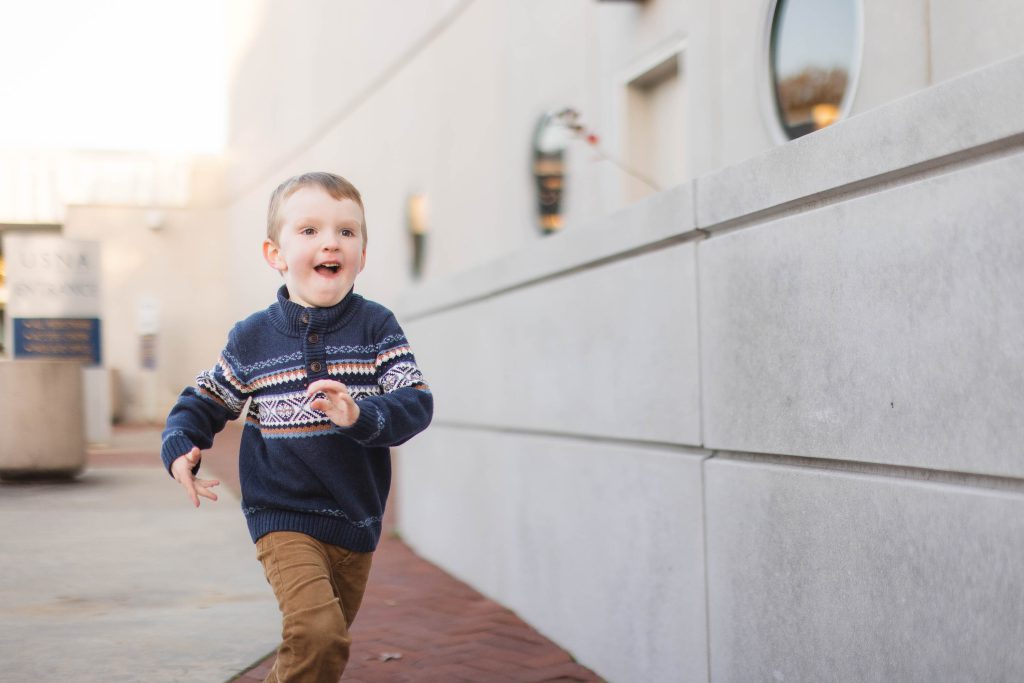 A young boy, part of a loving family, running down a sidewalk in downtown Annapolis with a smile on his face.