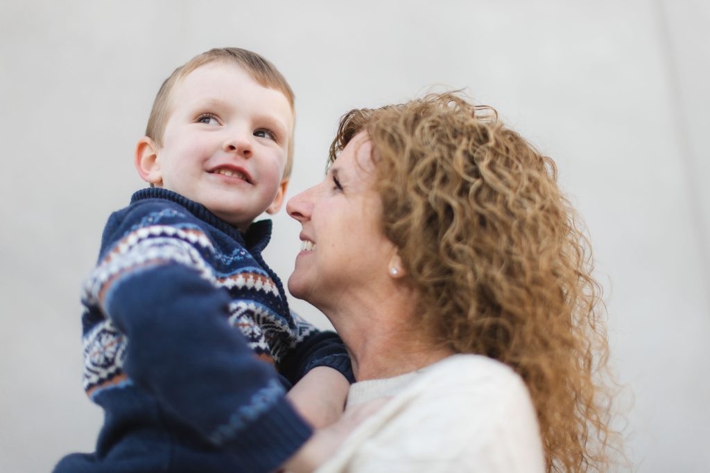 A family portrait of a woman holding a young boy in front of a gray wall.