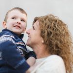 A family portrait of a woman holding a young boy in front of a gray wall.