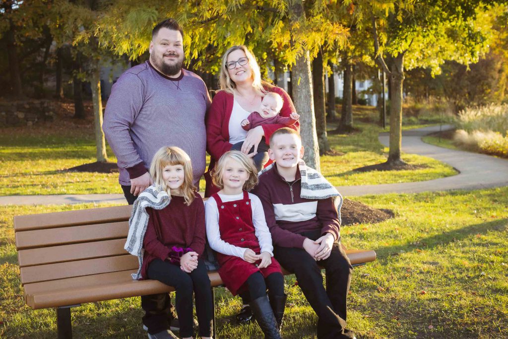 A family captures a beautiful sunset while sitting on a bench in a park, creating timeless portraits.