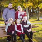 A family captures a beautiful sunset while sitting on a bench in a park, creating timeless portraits.