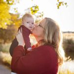 A woman holding a baby in her arms, capturing beautiful portraits of their family in a park during sunset.