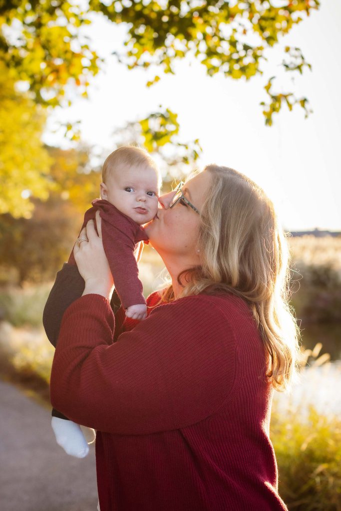 A woman holding a baby in her arms, capturing beautiful portraits of their family in a park during sunset.