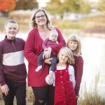A family is posing for a portrait in front of a serene pond during sunset.