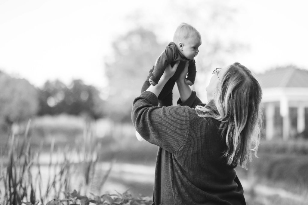 A black and white portrait of a woman holding her baby in the air.