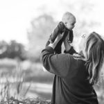 A black and white portrait of a woman holding her baby in the air.