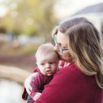 A woman embracing her baby in front of a peaceful pond at sunset, capturing heartwarming family portraits.