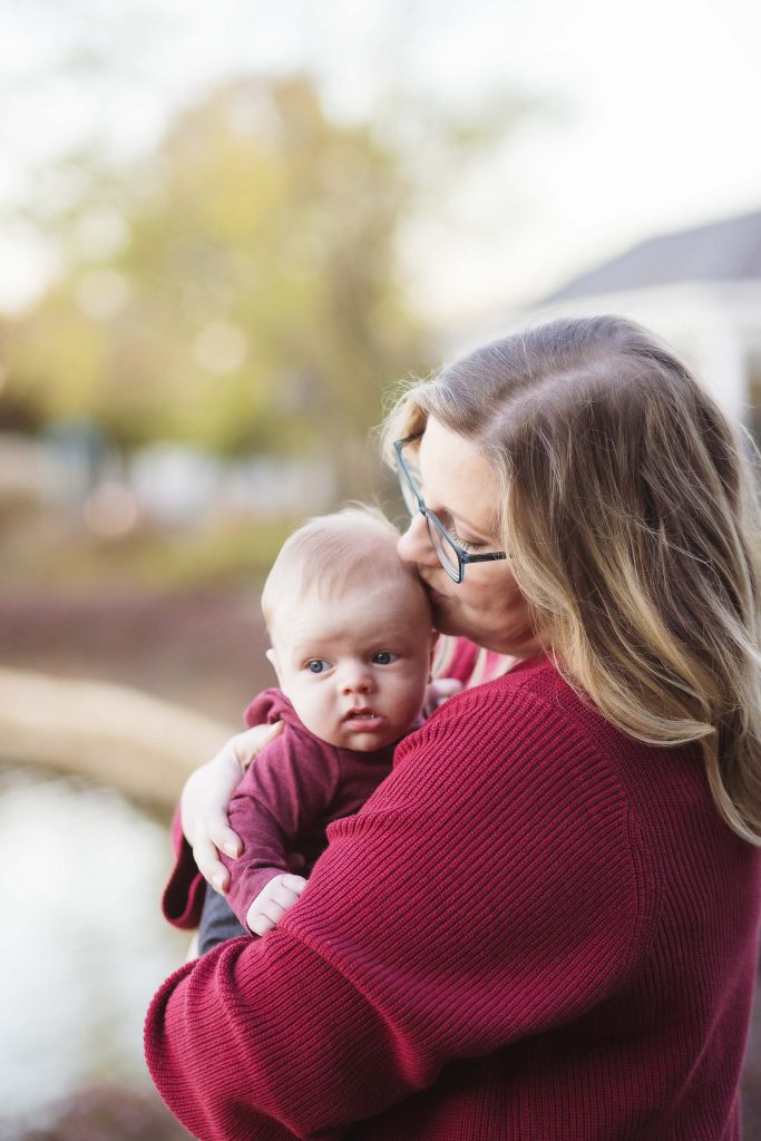 A woman embracing her baby in front of a peaceful pond at sunset, capturing heartwarming family portraits.