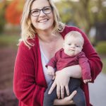 A woman in glasses holding a baby during sunset in a park, capturing beautiful family portraits.