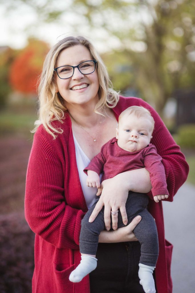 A woman in glasses holding a baby during sunset in a park, capturing beautiful family portraits.