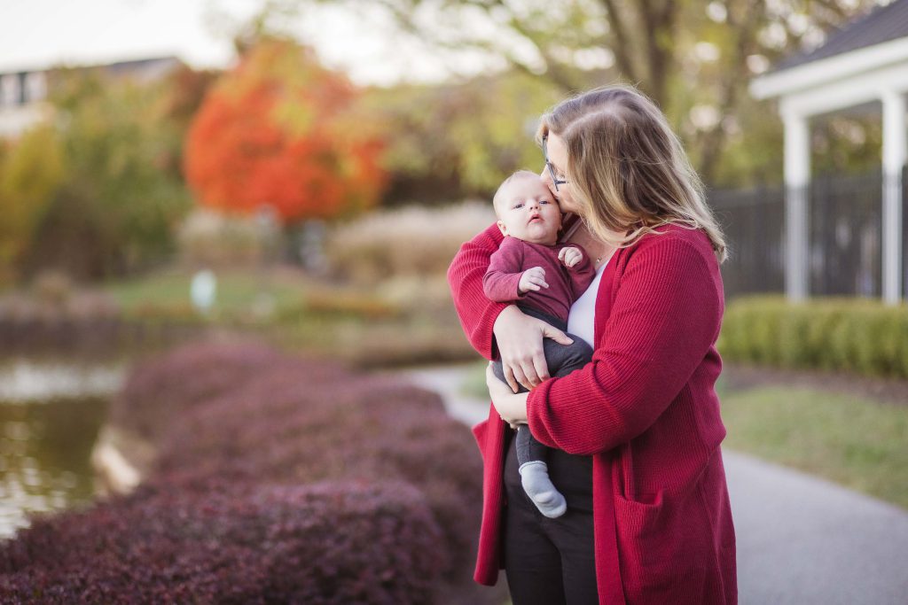 A woman holding a baby against the backdrop of a serene pond during sunset, capturing intimate family portraits.