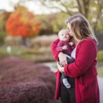 A woman holding a baby against the backdrop of a serene pond during sunset, capturing intimate family portraits.