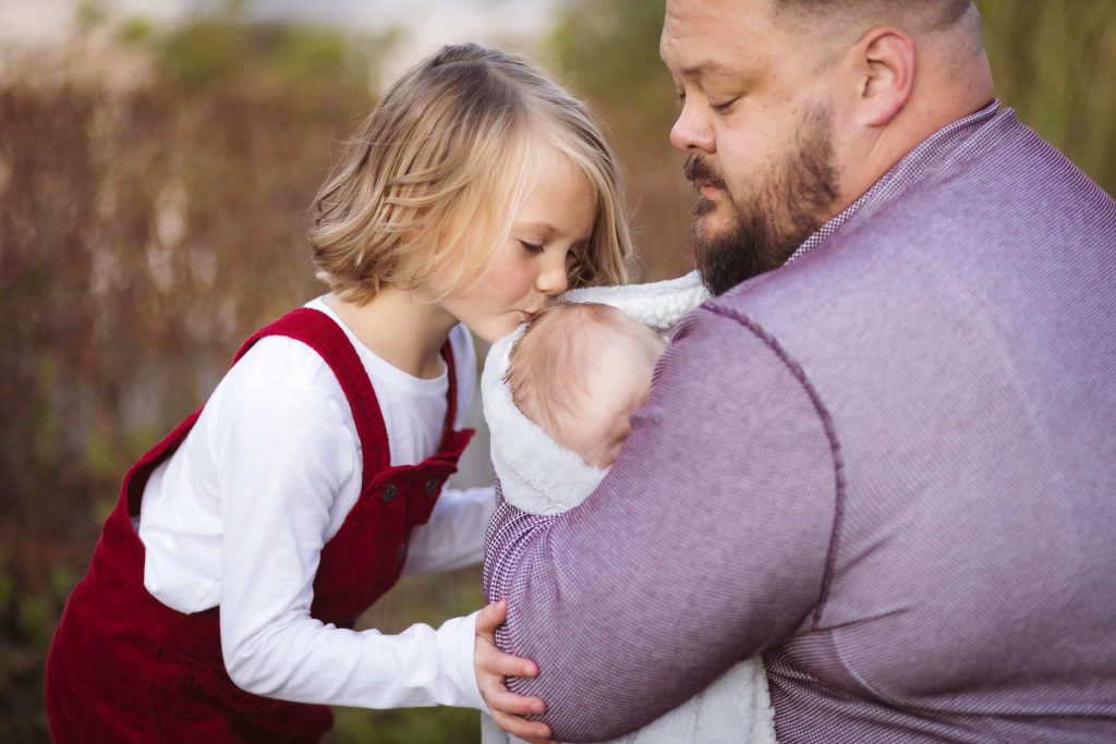 A man kisses a little girl in a family portrait at sunset.