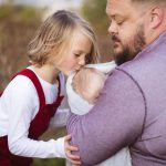 A man kisses a little girl in a family portrait at sunset.