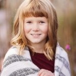 A little girl smiling while wrapped in a blanket during a sunset.