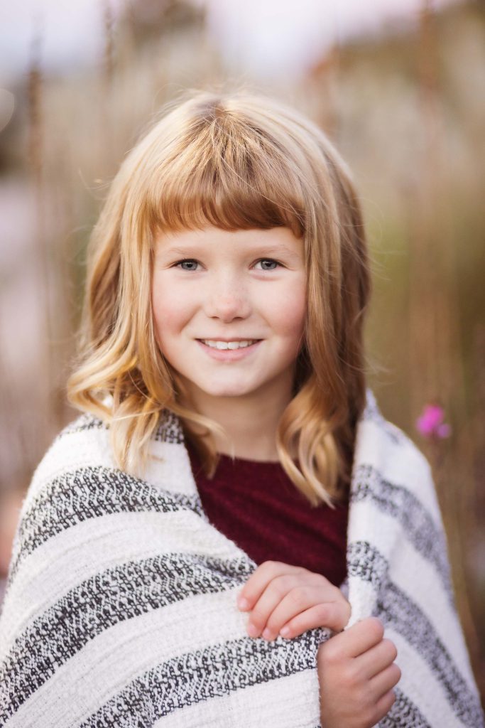 A little girl smiling while wrapped in a blanket during a sunset.