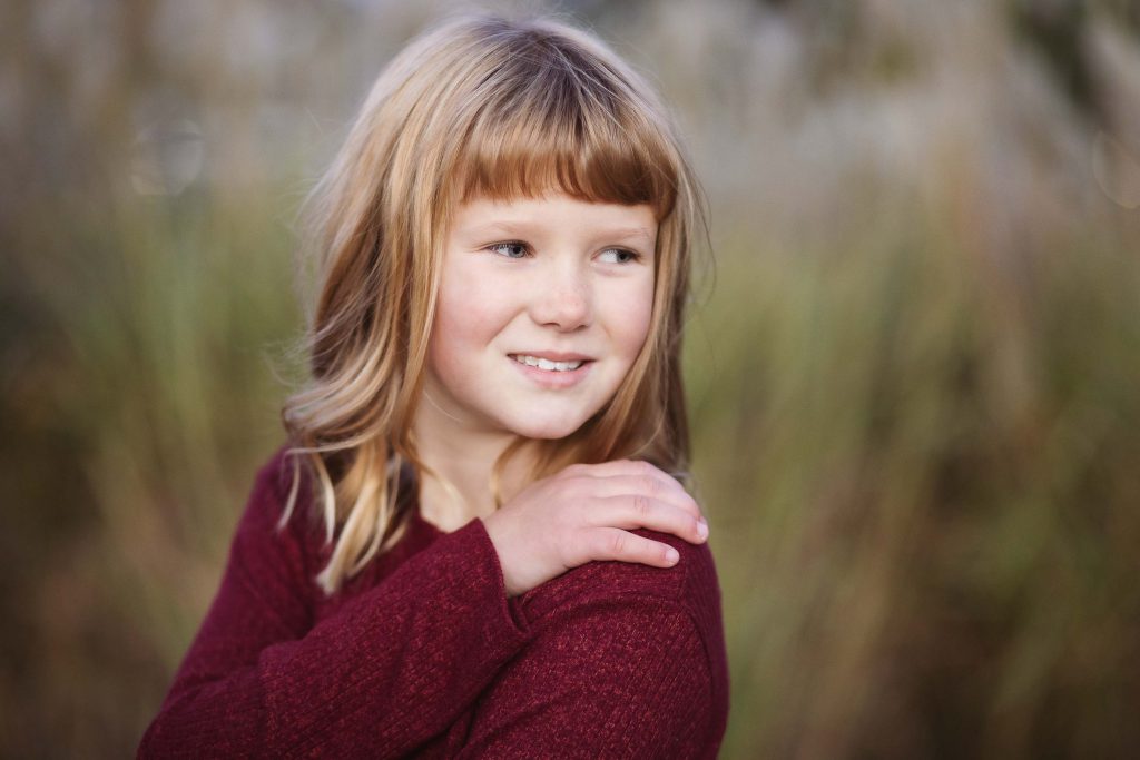 A little girl is posing for a family portrait in a field at sunset.