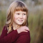 A little girl is posing for a family portrait in a field at sunset.