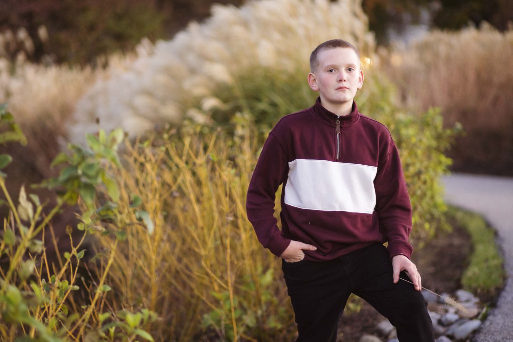 A young boy in a maroon and black sweater standing on a path during sunset.