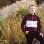 A young boy in a maroon and black sweater standing on a path during sunset.
