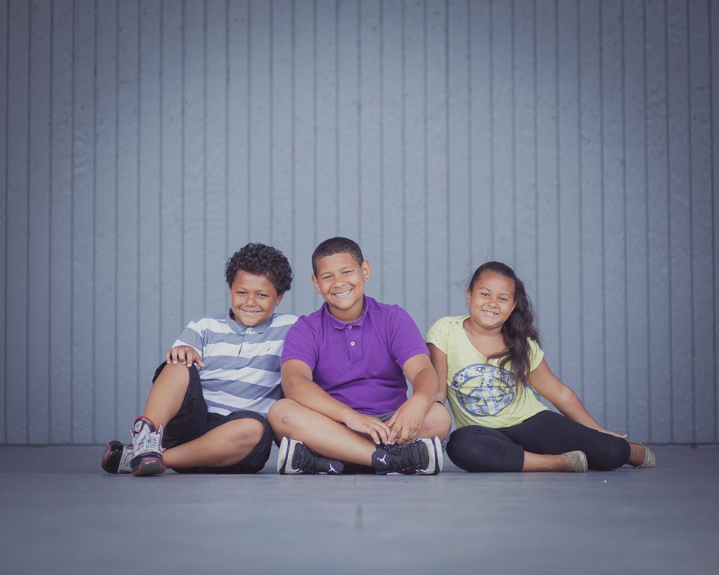 Three children sitting on the floor in front of a gray wall at Allen Pond in Bowie, Maryland.
