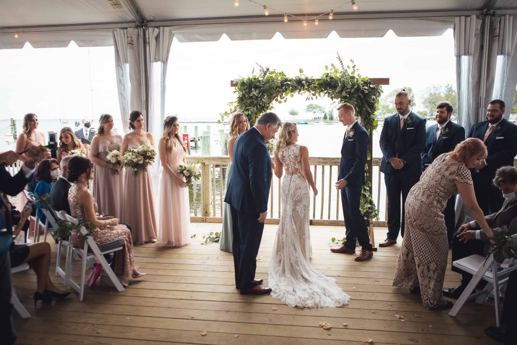 A wedding ceremony on the Annapolis Maritime Museum deck in Annapolis, Maryland with a bride and groom.