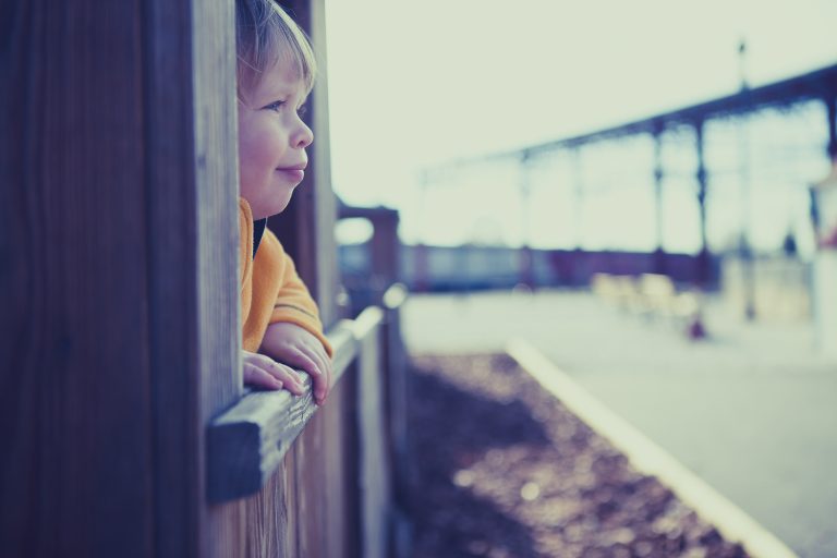 A young boy looking out of a wooden fence at the B&O Railroad Museum in Baltimore, Maryland.