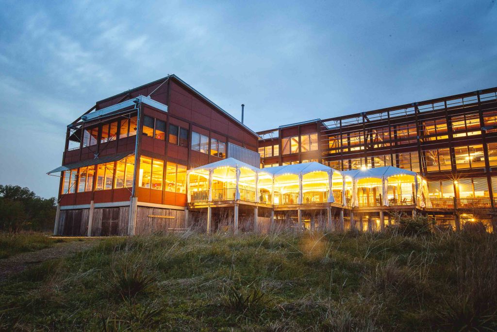 A large building lit up at dusk in the middle of a grassy field near Chesapeake Bay Foundation in Maryland.