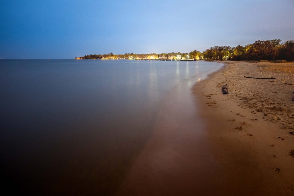 A beach at dusk in Annapolis, Maryland with a light shining on it.