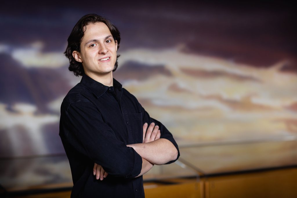 A young man with his arms crossed in front of a painting at the College Park Aviation Museum.