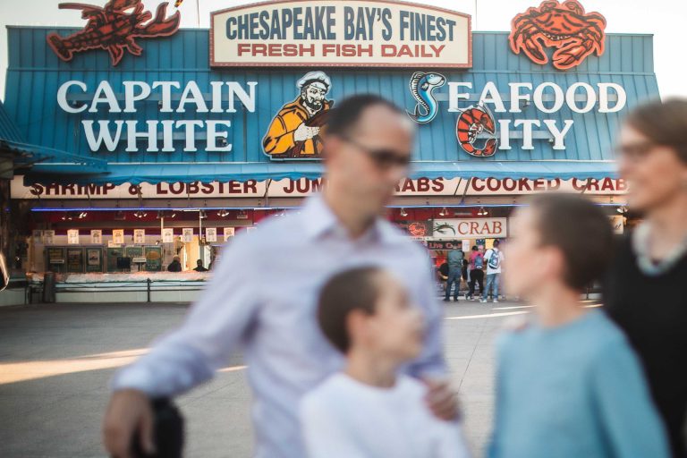 A family walks past a sign for District Wharf in Washington DC, featuring Captain Seafood White.