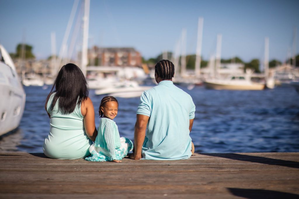 A family sits on a dock in Downtown Annapolis with boats in the background.