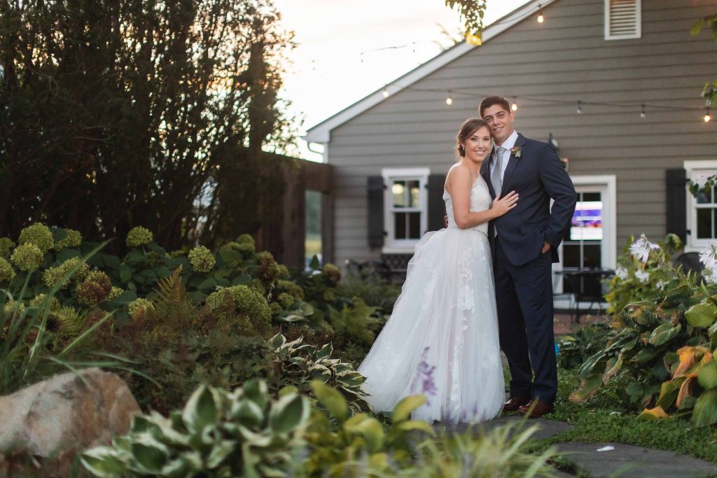 A bride and groom pose for a photo in front of a garden at Fleetwood Farm Winery in Leesburg, Virginia.