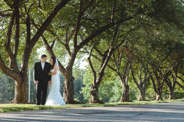 A bride and groom standing under trees at Glenview Mansion in Maryland.