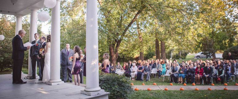 A historic wedding ceremony on the porch of Maryland's Historic Baldwin Hall in Millersville, with a large group of people.