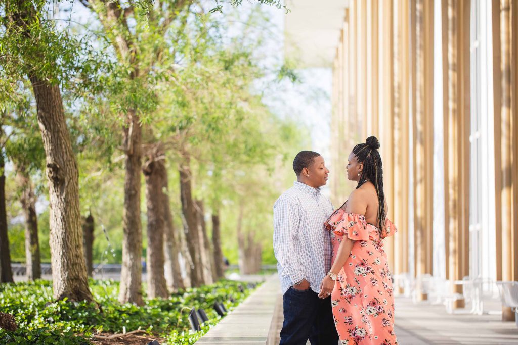 An engaged couple standing in front of the Kennedy Center Grounds building.