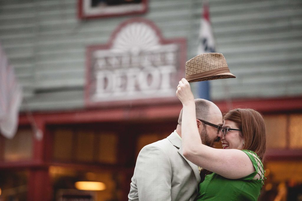 A man and woman hugging in front of a store in Old Ellicott City with a hat.