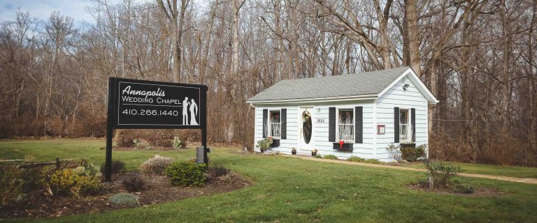 A small white building for the Annapolis Wedding Chapel with a sign out front and winter trees in the background.