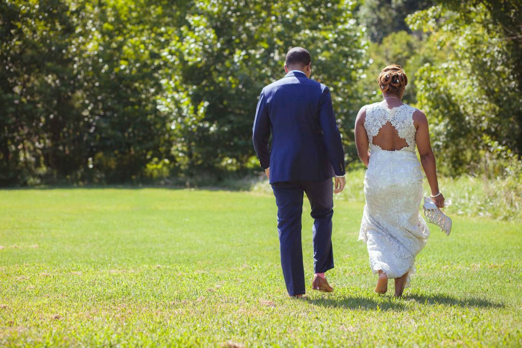 A bride and groom walking through a grassy field near Great Seneca Lodge in Maryland, Germantown.