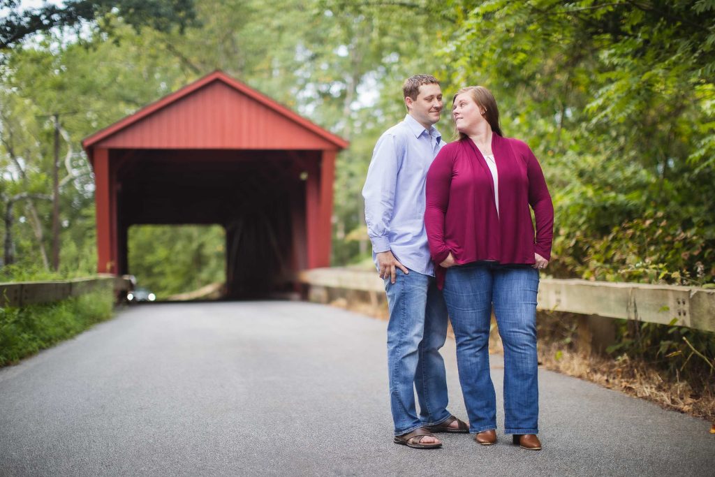 An engaged couple standing in front of Jerusalem Mill, a covered bridge in Maryland near Bel Air.