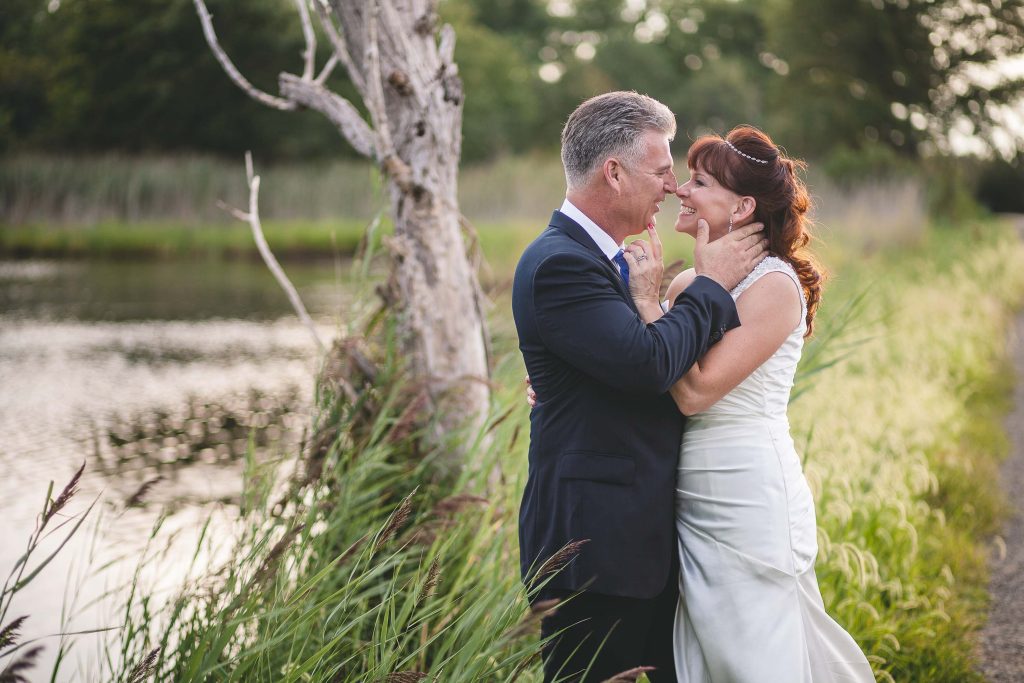 A bride and groom hugging near a pond in Terrapin Nature Park.
