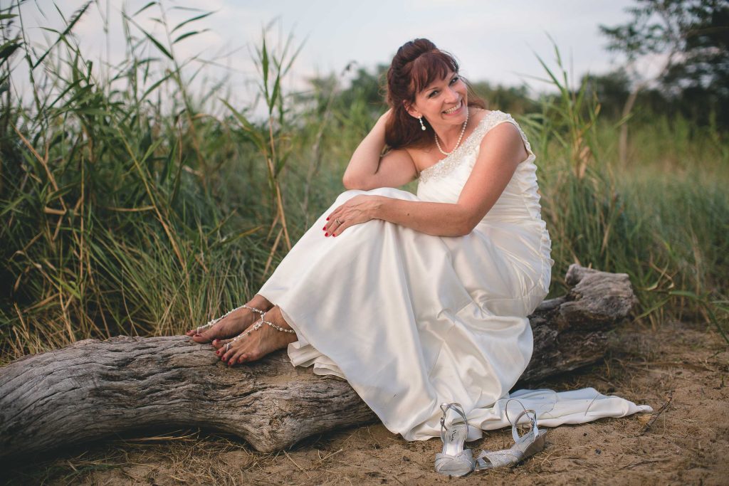A bride sitting on a log at Terrapin Nature Park in Maryland.